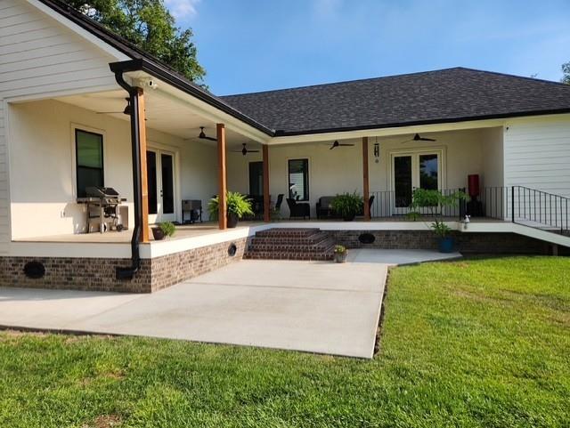 rear view of house with a shingled roof, a patio, ceiling fan, and a yard