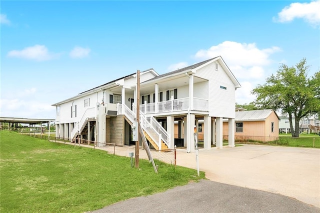 rear view of property with a porch, stairs, concrete driveway, a lawn, and a carport