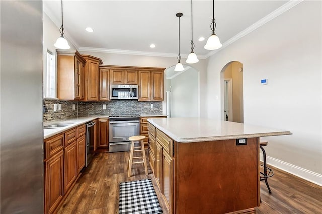 kitchen with a breakfast bar, a center island, brown cabinets, arched walkways, and stainless steel appliances
