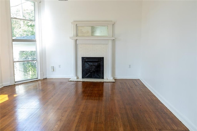 unfurnished living room featuring baseboards, a brick fireplace, and dark wood-style floors