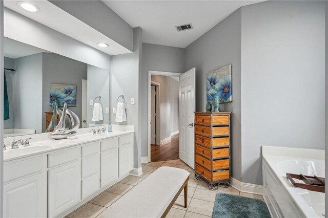 bathroom with a sink, double vanity, baseboards, visible vents, and a garden tub