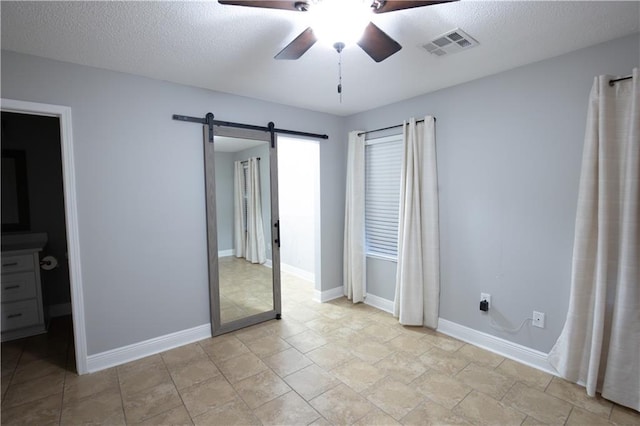 unfurnished bedroom featuring a textured ceiling, baseboards, visible vents, and a barn door