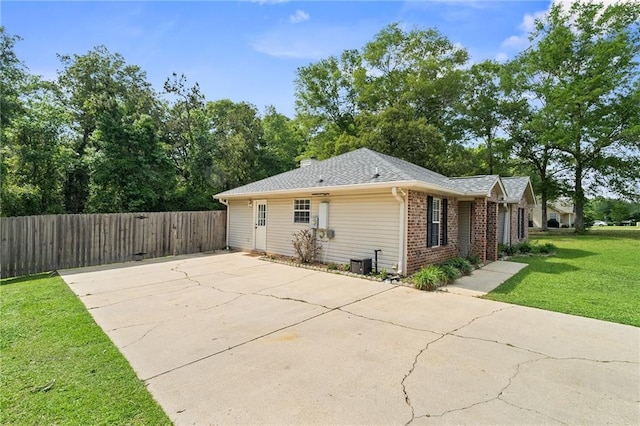 view of property exterior featuring driveway, brick siding, central AC, fence, and a yard