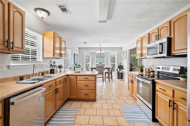 kitchen with visible vents, a peninsula, a textured ceiling, a sink, and stainless steel appliances
