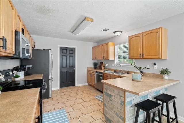 kitchen with a sink, stainless steel appliances, a peninsula, a kitchen bar, and visible vents