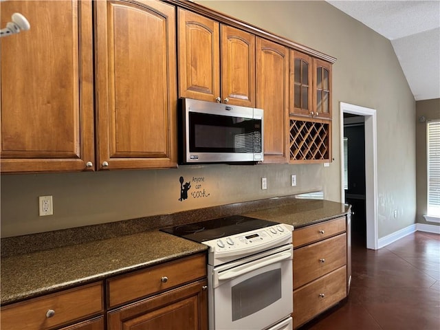 kitchen with stainless steel microwave, white electric range oven, brown cabinetry, and vaulted ceiling