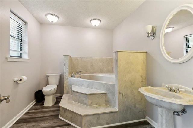 full bath with a garden tub, wood finished floors, toilet, baseboards, and a textured ceiling