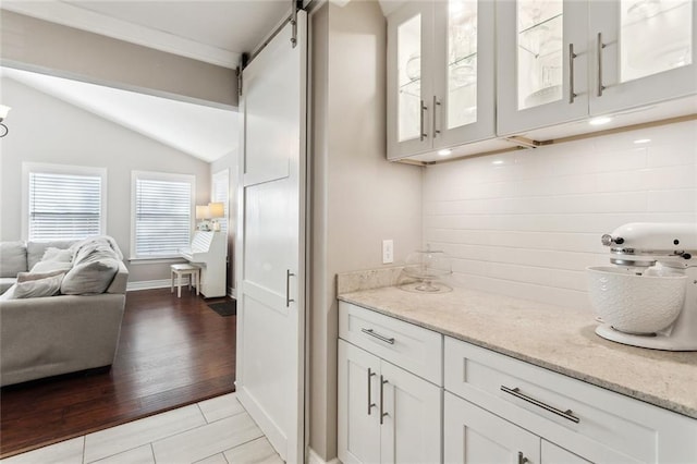 bar featuring baseboards, vaulted ceiling, a barn door, and light tile patterned floors