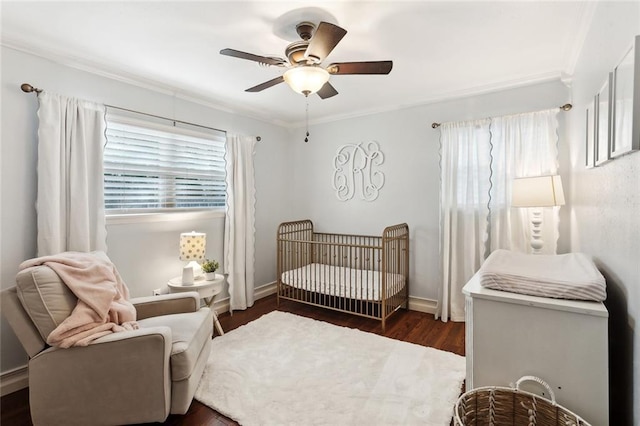 bedroom featuring ceiling fan, ornamental molding, a crib, and dark wood-type flooring