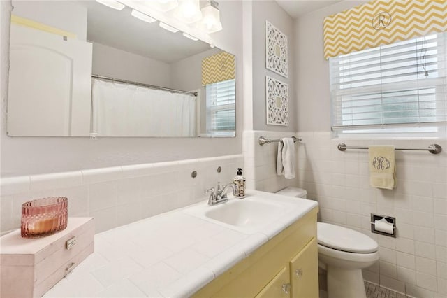 bathroom with wainscoting, a healthy amount of sunlight, toilet, and tile walls