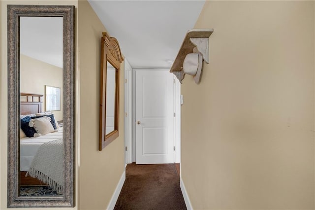 hall with baseboards and dark carpet