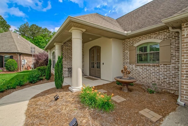 property entrance featuring brick siding, a shingled roof, and stucco siding