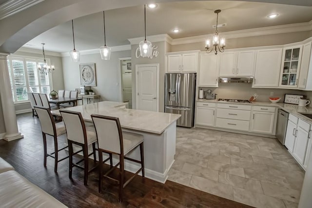 kitchen with ornamental molding, under cabinet range hood, a chandelier, arched walkways, and appliances with stainless steel finishes