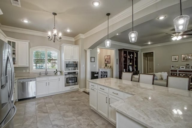 kitchen featuring appliances with stainless steel finishes, a sink, white cabinetry, decorative columns, and ornamental molding