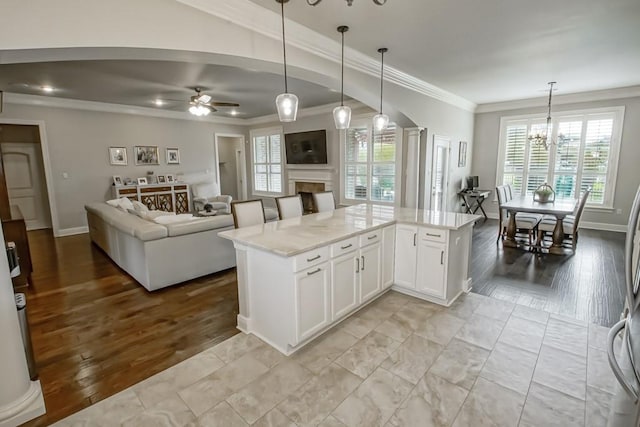 kitchen featuring ornamental molding, light stone countertops, a fireplace, open floor plan, and ceiling fan with notable chandelier