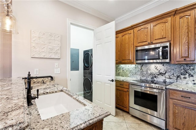 kitchen featuring stacked washer and dryer, appliances with stainless steel finishes, a sink, and light stone counters