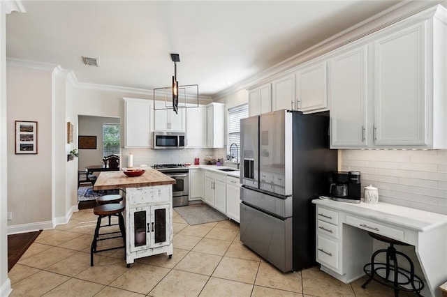 kitchen with crown molding, appliances with stainless steel finishes, butcher block countertops, a kitchen bar, and visible vents