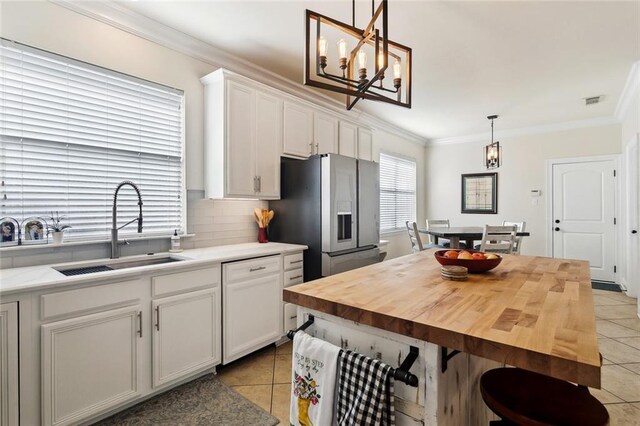 kitchen with light tile patterned floors, ornamental molding, a sink, and stainless steel refrigerator with ice dispenser