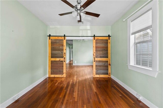 empty room featuring baseboards, ceiling fan, wood-type flooring, and a barn door