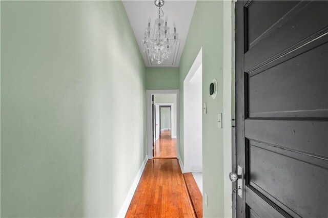 corridor featuring an inviting chandelier, baseboards, attic access, and wood finished floors