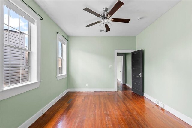 spare room with wood-type flooring, a ceiling fan, baseboards, and visible vents