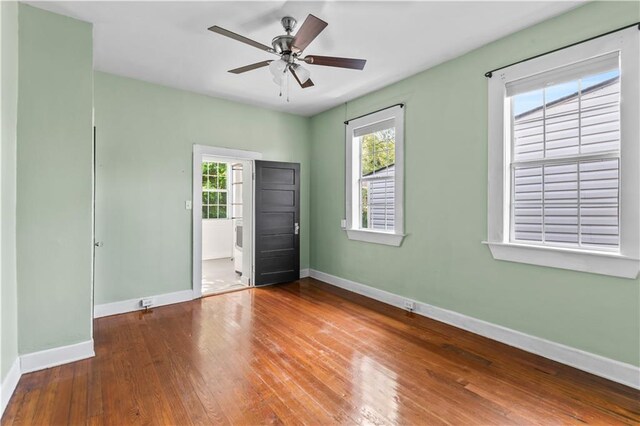 unfurnished bedroom with baseboards, multiple windows, a ceiling fan, and hardwood / wood-style floors