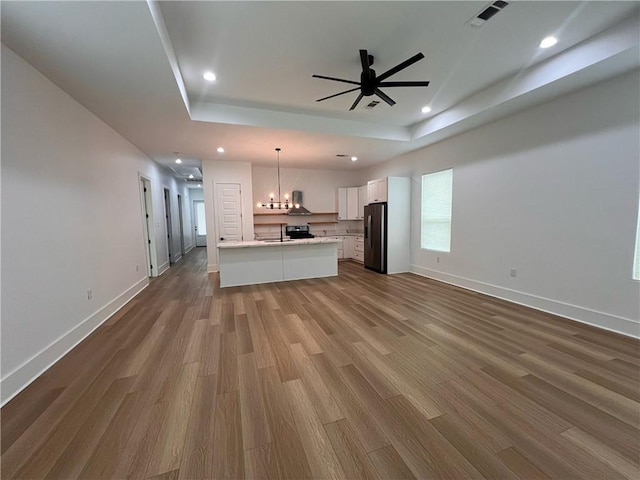 unfurnished living room with wood finished floors, recessed lighting, a tray ceiling, a sink, and ceiling fan with notable chandelier