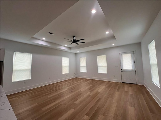 unfurnished living room featuring a raised ceiling, plenty of natural light, a ceiling fan, wood finished floors, and visible vents