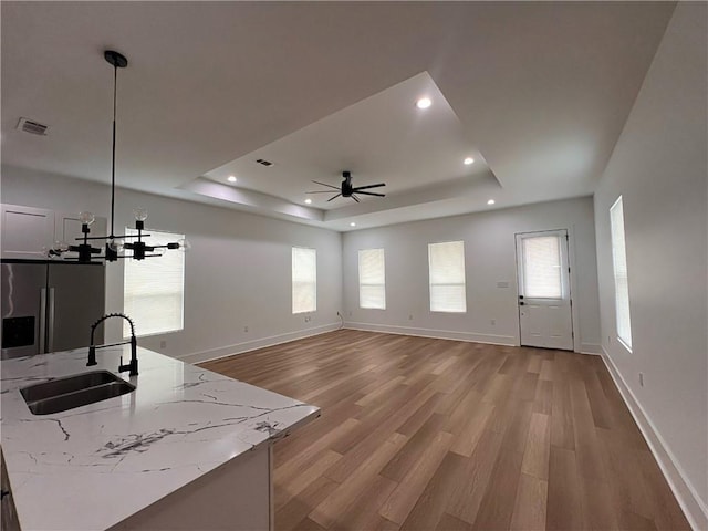 unfurnished living room with visible vents, a sink, a raised ceiling, and light wood-style flooring