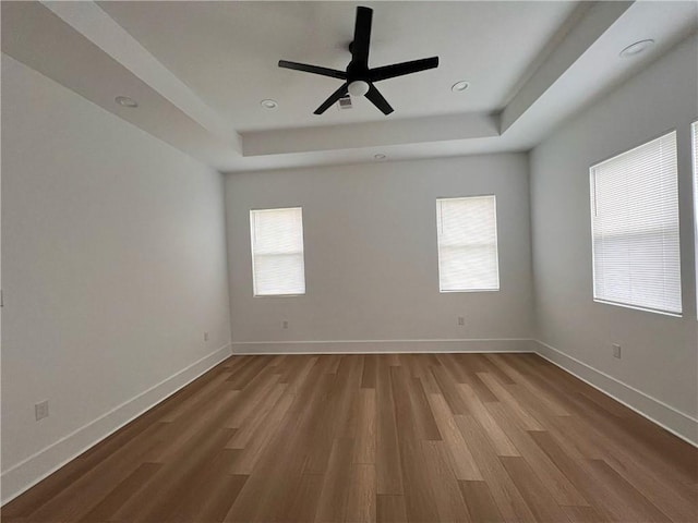 empty room with baseboards, ceiling fan, a tray ceiling, and wood finished floors