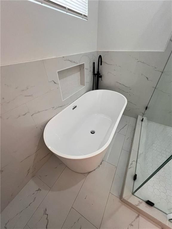 bathroom with a freestanding tub, tile walls, wainscoting, and marble finish floor