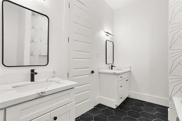 bathroom featuring tile patterned flooring, a sink, baseboards, and two vanities