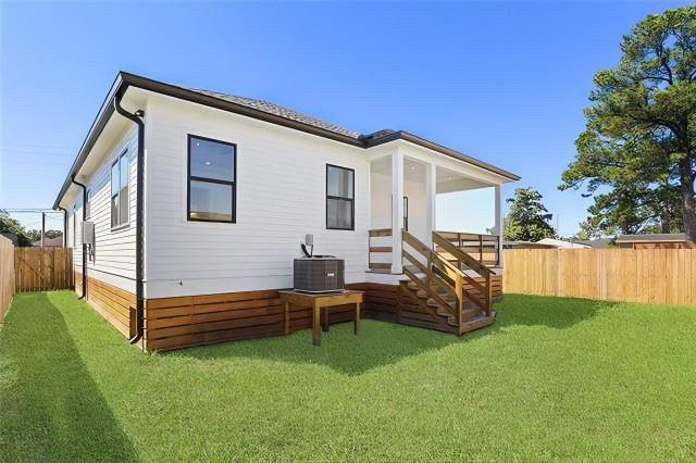 back of house featuring a fenced backyard, central AC unit, and a yard