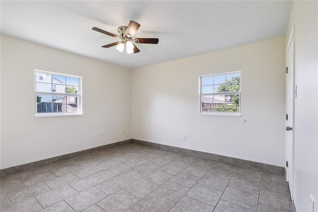 tiled empty room with ceiling fan and baseboards