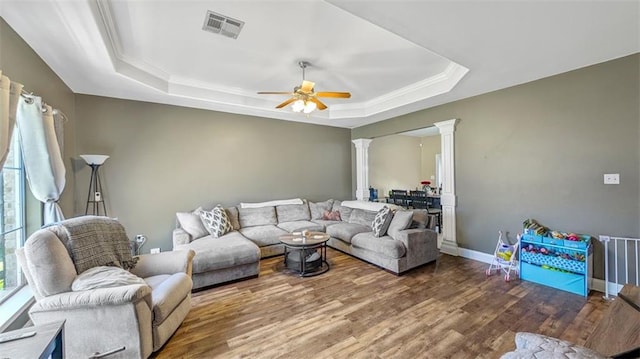 living room featuring visible vents, decorative columns, wood finished floors, a tray ceiling, and a ceiling fan