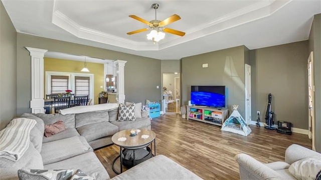 living room featuring a raised ceiling, decorative columns, ceiling fan, and wood finished floors