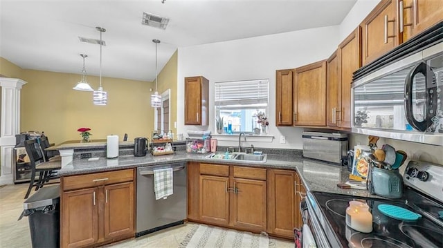 kitchen with a sink, appliances with stainless steel finishes, a peninsula, and brown cabinets