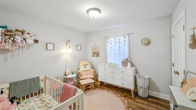 bedroom featuring baseboards, a crib, and wood finished floors