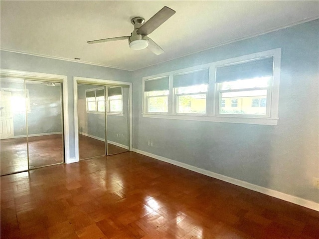 unfurnished bedroom with baseboards, ceiling fan, and two closets