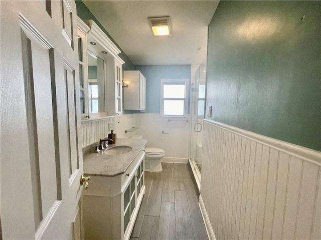 bathroom featuring wainscoting, vanity, toilet, wood finished floors, and a stall shower