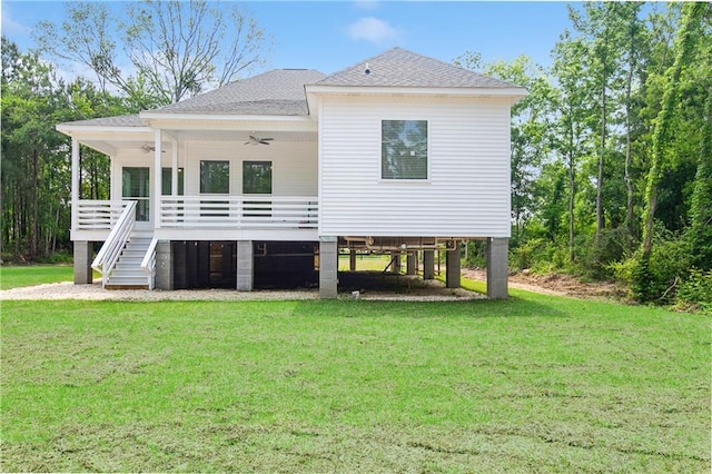 rear view of house featuring ceiling fan, a deck, stairs, a shingled roof, and a lawn