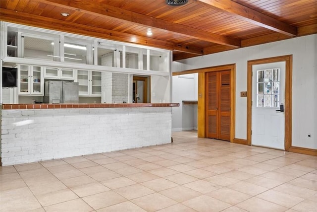 unfurnished living room featuring light tile patterned flooring, brick wall, beamed ceiling, baseboards, and wood ceiling