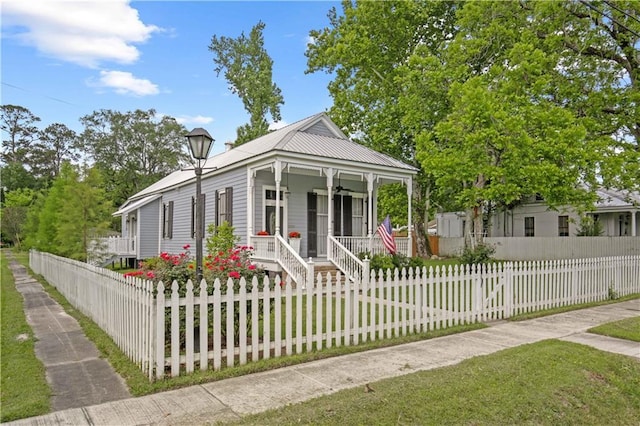 shotgun-style home featuring a porch, ceiling fan, a fenced front yard, and metal roof