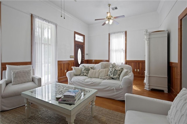 living room featuring a wainscoted wall, ceiling fan, wood finished floors, and visible vents