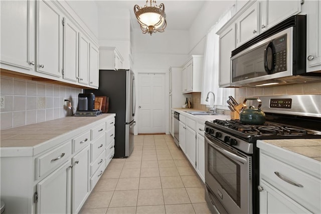 kitchen with backsplash, a sink, light tile patterned floors, white cabinets, and stainless steel appliances
