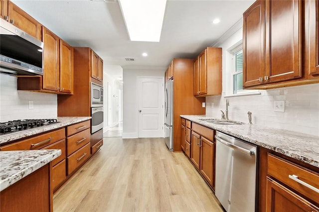 kitchen with a sink, light stone countertops, stainless steel appliances, and light wood-style flooring