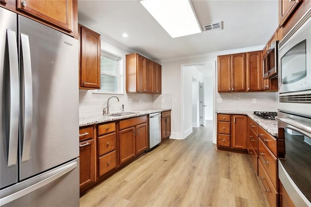 kitchen with brown cabinets, a sink, light wood finished floors, stainless steel appliances, and backsplash