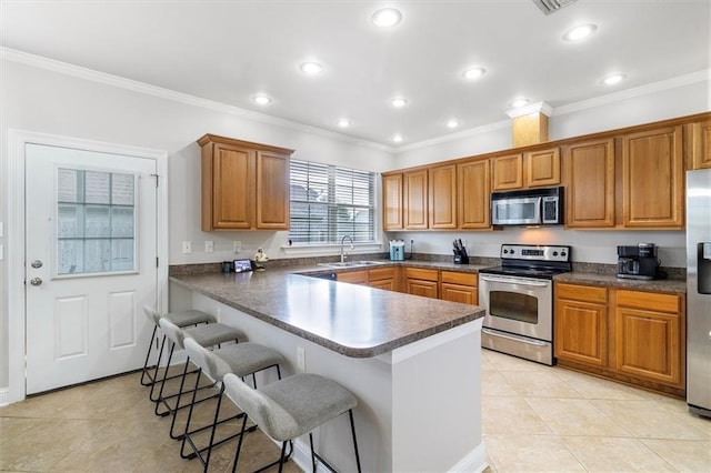kitchen with brown cabinets, light tile patterned flooring, appliances with stainless steel finishes, a sink, and a kitchen breakfast bar