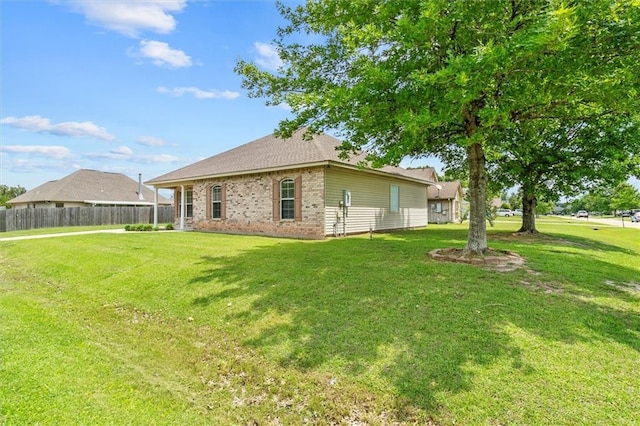 rear view of house featuring fence, a lawn, and brick siding