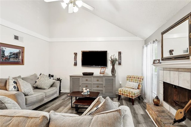 living room featuring a tiled fireplace, high vaulted ceiling, wood finished floors, and visible vents